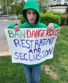 Boy, Q.T., photographed holding sign that says, "Ban dangerous restraint and seclusion"