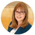 Eve Hill headshot. White woman with medium length red hair and dark rimmed glasses smiling.