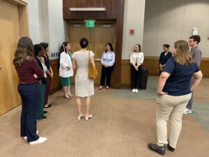 Staff members of the National Federation of the Blind give a group of Brown, Goldstein & Levy attorneys and staff members a tour of the National Federation of the Blind headquarters in Baltimore, MD. The group, dressed business casual, is standing in a circle in a hallway listening to someone speak.