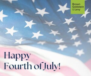 A close-up of the United States flag with text that reads "Happy Fourth of July!" in navy blue text. In the top right corner, a green square displays the logo of Brown, Goldstein & Levy.
