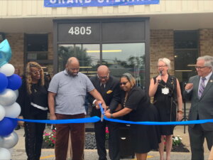 Group of people happily cutting ribbon together in front of building entrance.