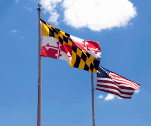 Maryland state flag and the United States flag on flagpoles against a blue sky with a few bright white clouds.