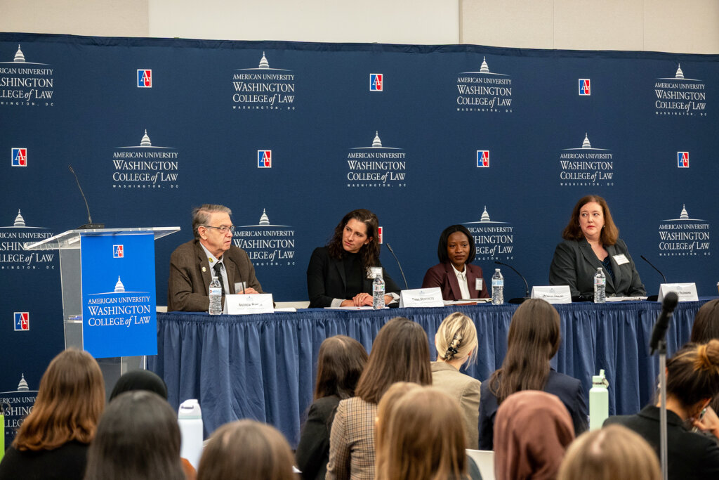A panel of four people sitting at a table. Michelle Fraling is second from the right and is wearing a brown blazer and white shirt.